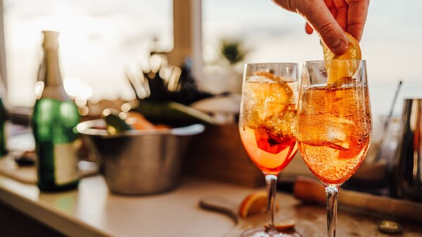 Two glasses of a cocktail with ice cubes and a slice of orange garnish, a bottle, and a metal bucket on a bar counter. - Grand Hotel Heiligendamm (Bad Doberan)