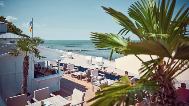 A beachside bar with outdoor seating, a flag, and a view of the ocean. - Grand Hotel Heiligendamm (Bad Doberan)