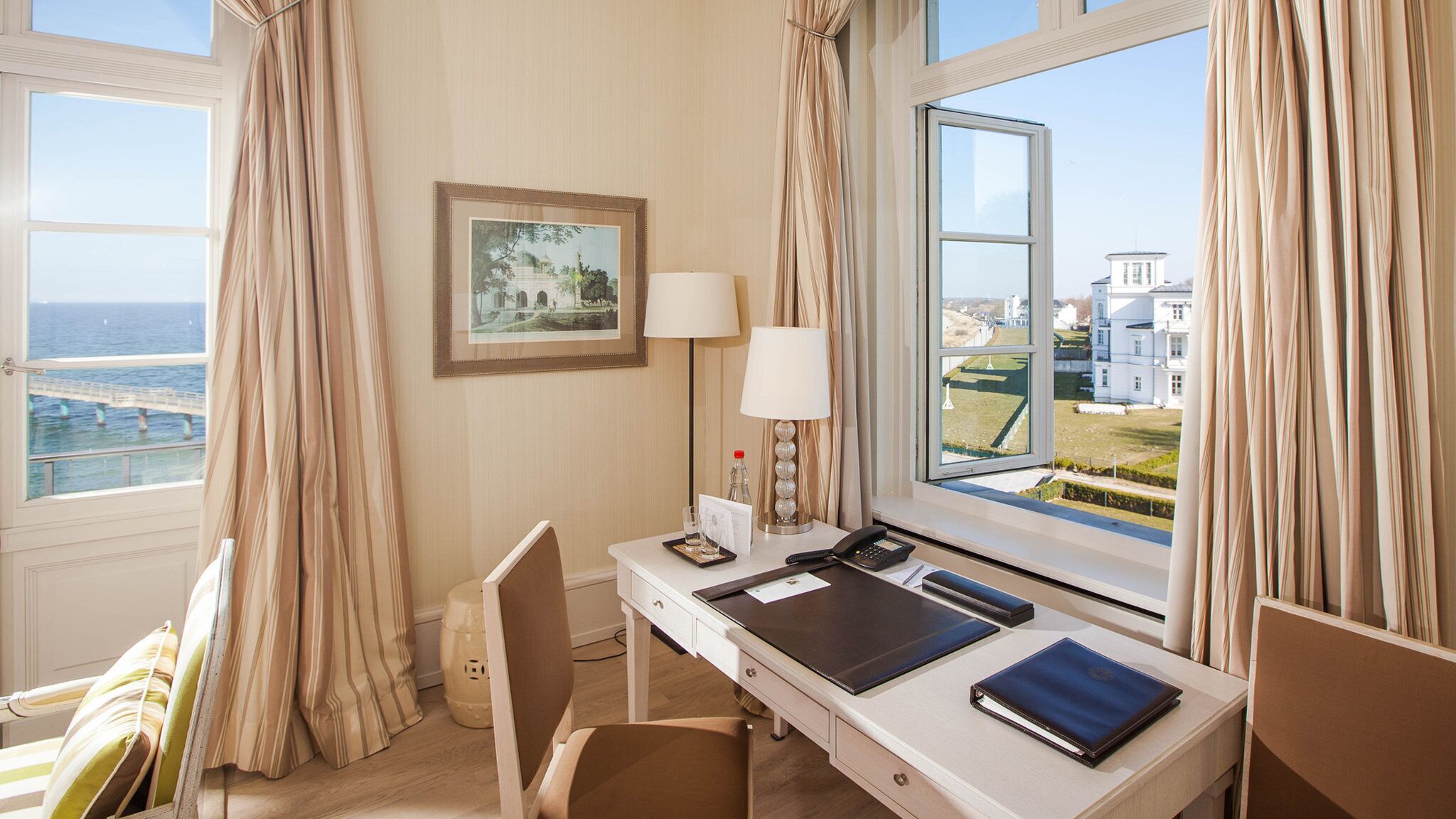Habitación de hotel con escritorio, una silla, lámpara, teléfono y un cuadro en la pared.