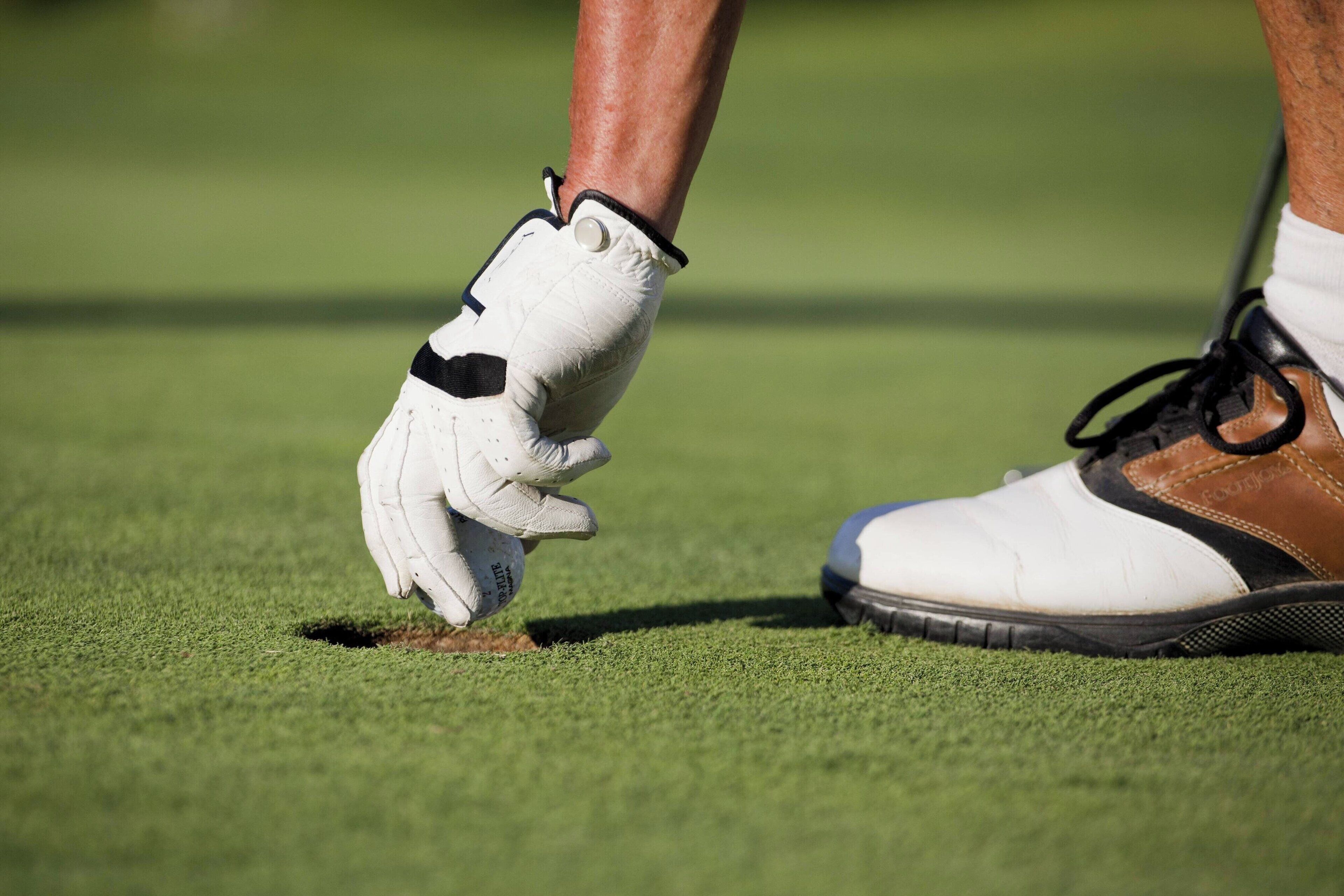 Primer plano de un guante y un zapato de golf sobre una superficie verde.
