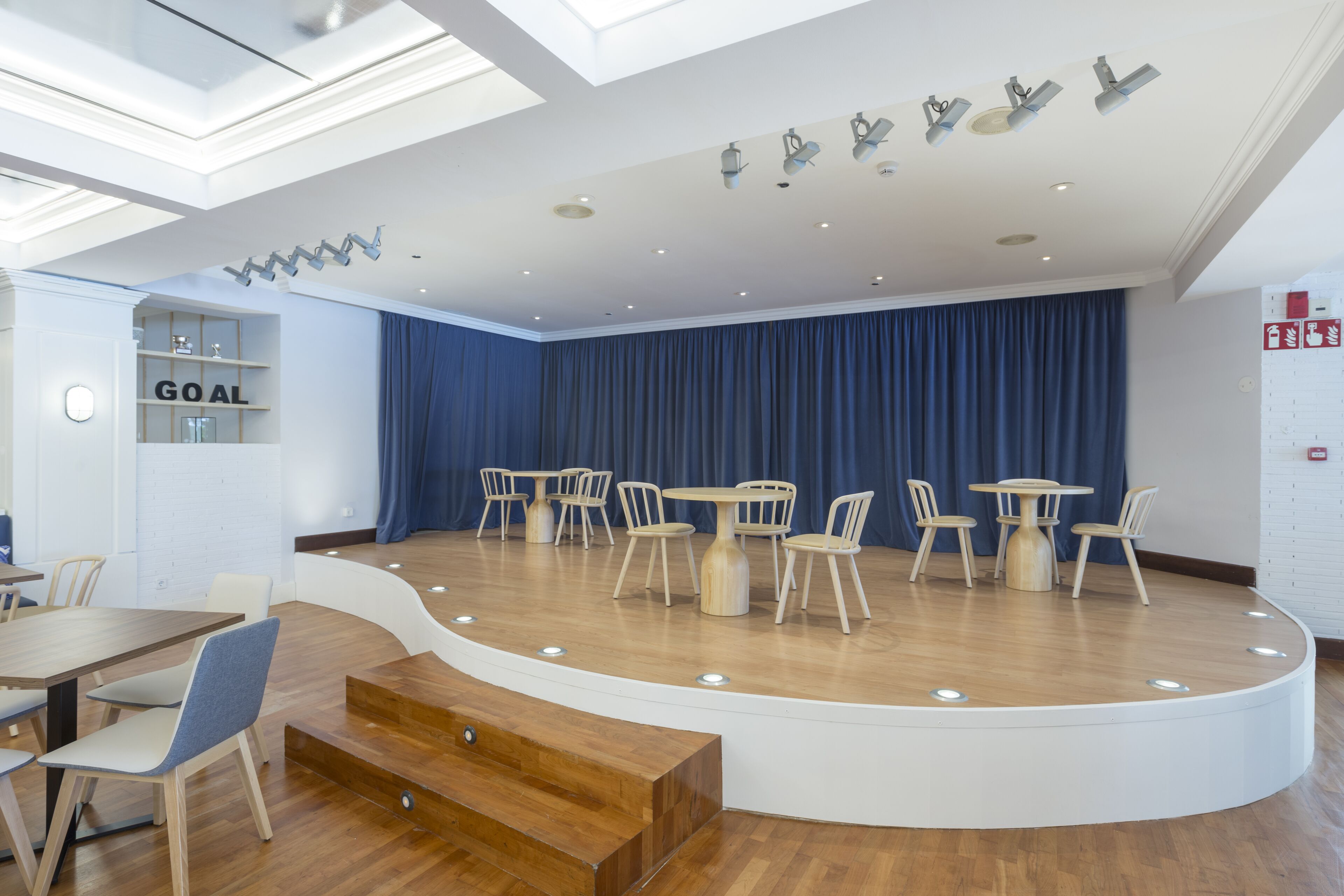 A modern conference room with a stage, round tables, and chairs.