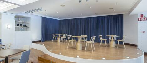 A modern conference room with a stage, round tables, and chairs.