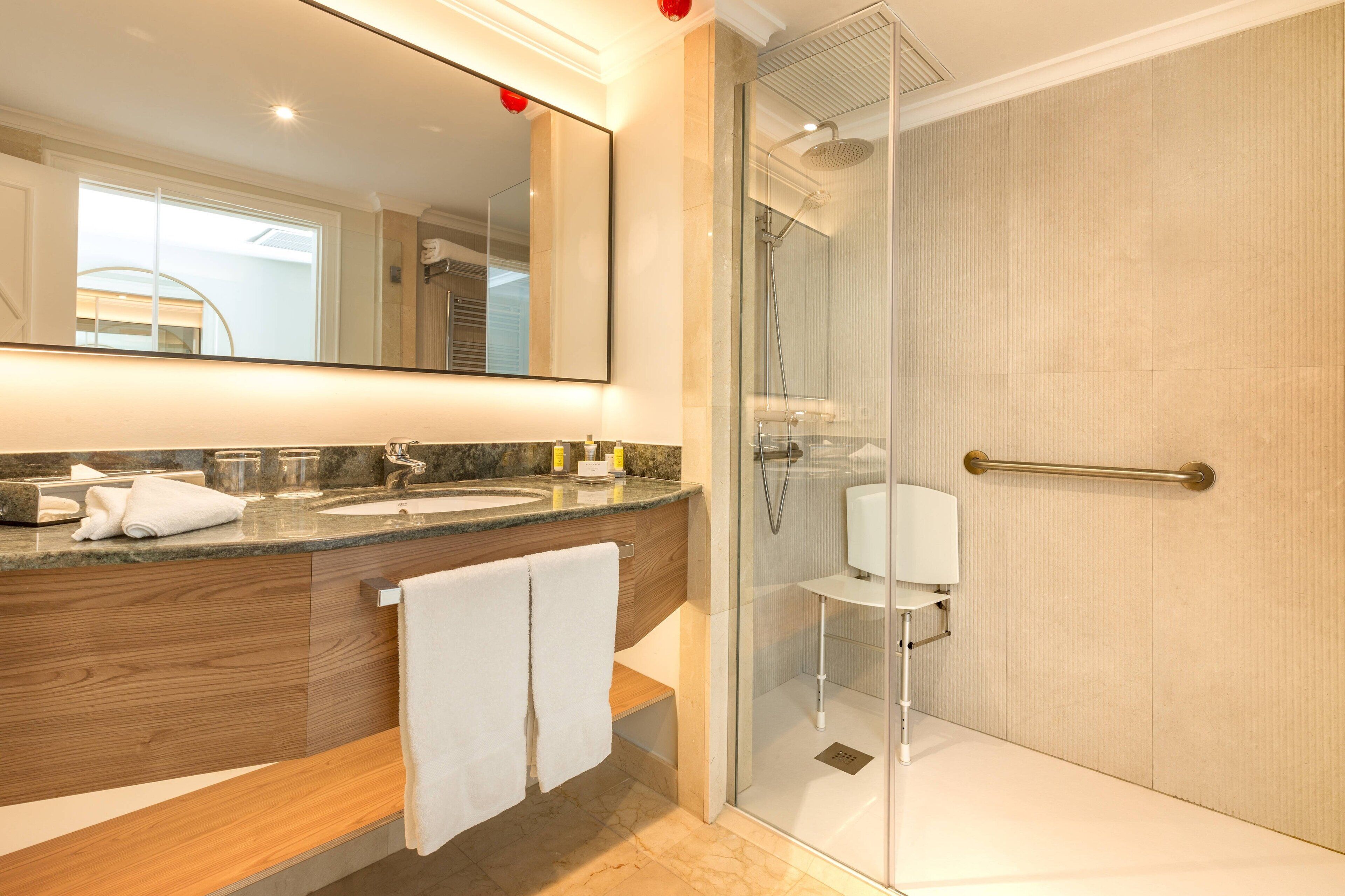 Un baño moderno con ducha envuelta en vidrio, un espejo grande y un mueble de tocador de madera.