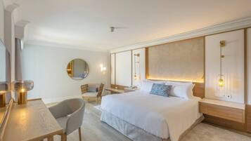 Una camera d'albergo moderna con un letto grande, una scrivania con una sedia, uno specchio rotondo e un comodino con una lampada.