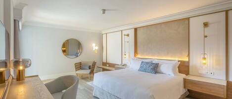 Una habitación de hotel moderna con una cama grande, un escritorio con silla, un espejo redondo y una mesita de noche con lámpara.