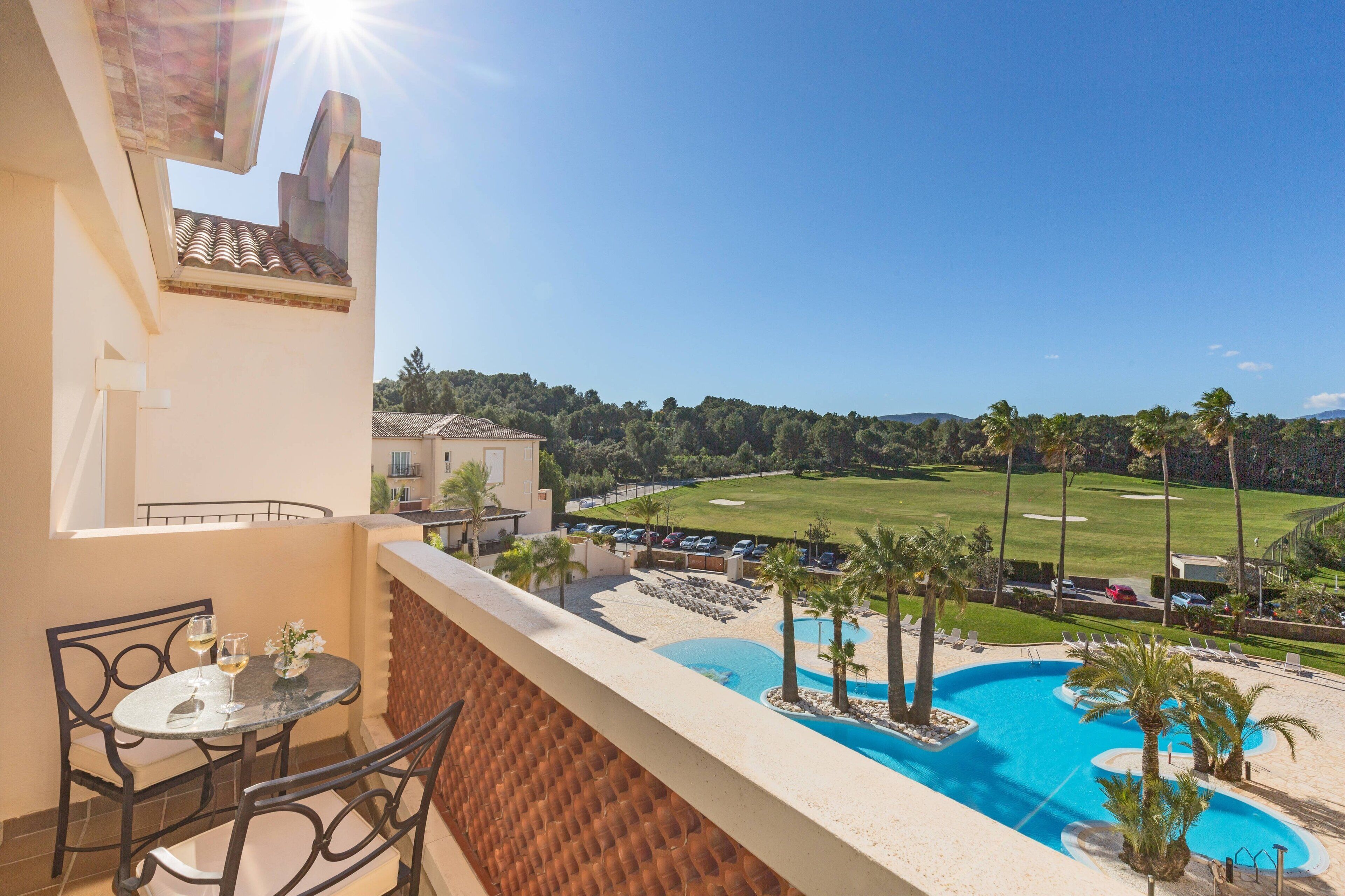 A balcony with a view of a swimming pool, palm trees, and a golf course.