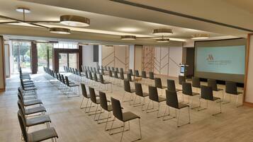 Un salón de conferencias con filas de sillas, una pantalla grande mostrando el logotipo de Marriott y un diseño moderno en el techo.