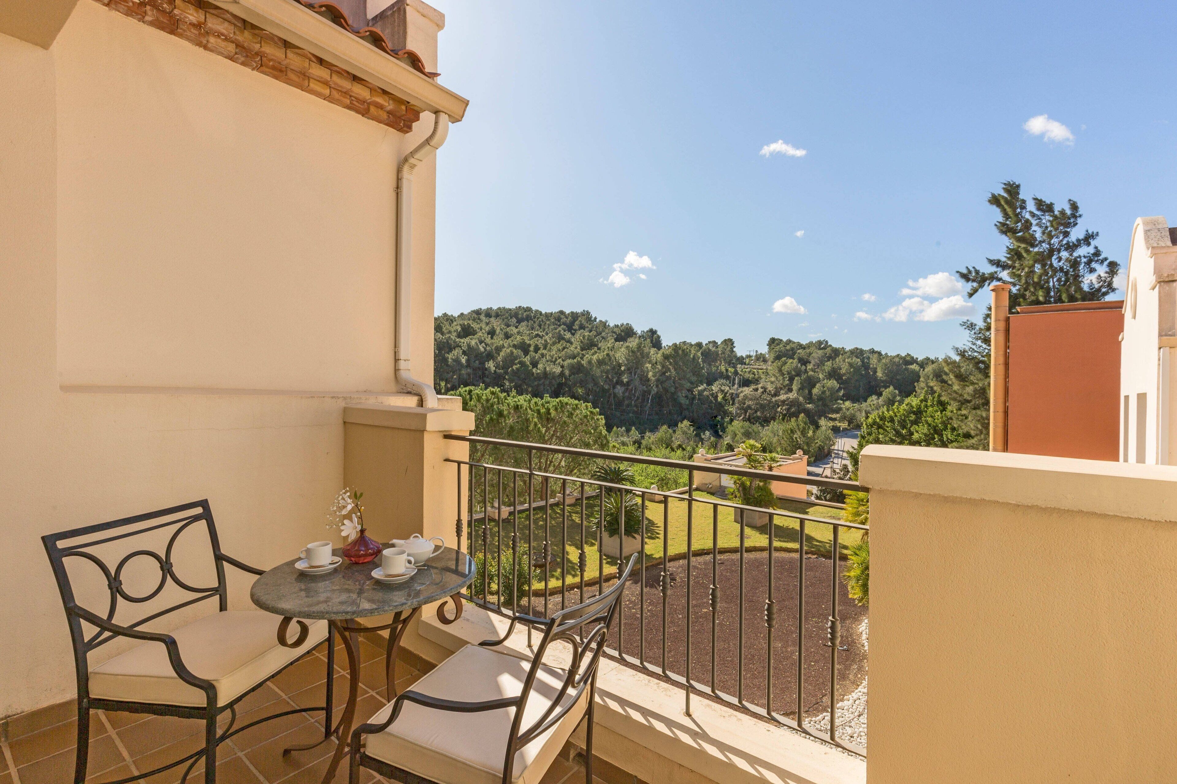 Ein Balkon mit Tisch und Stühlen, der Blick auf eine grüne Landschaft und Bäume bietet.
