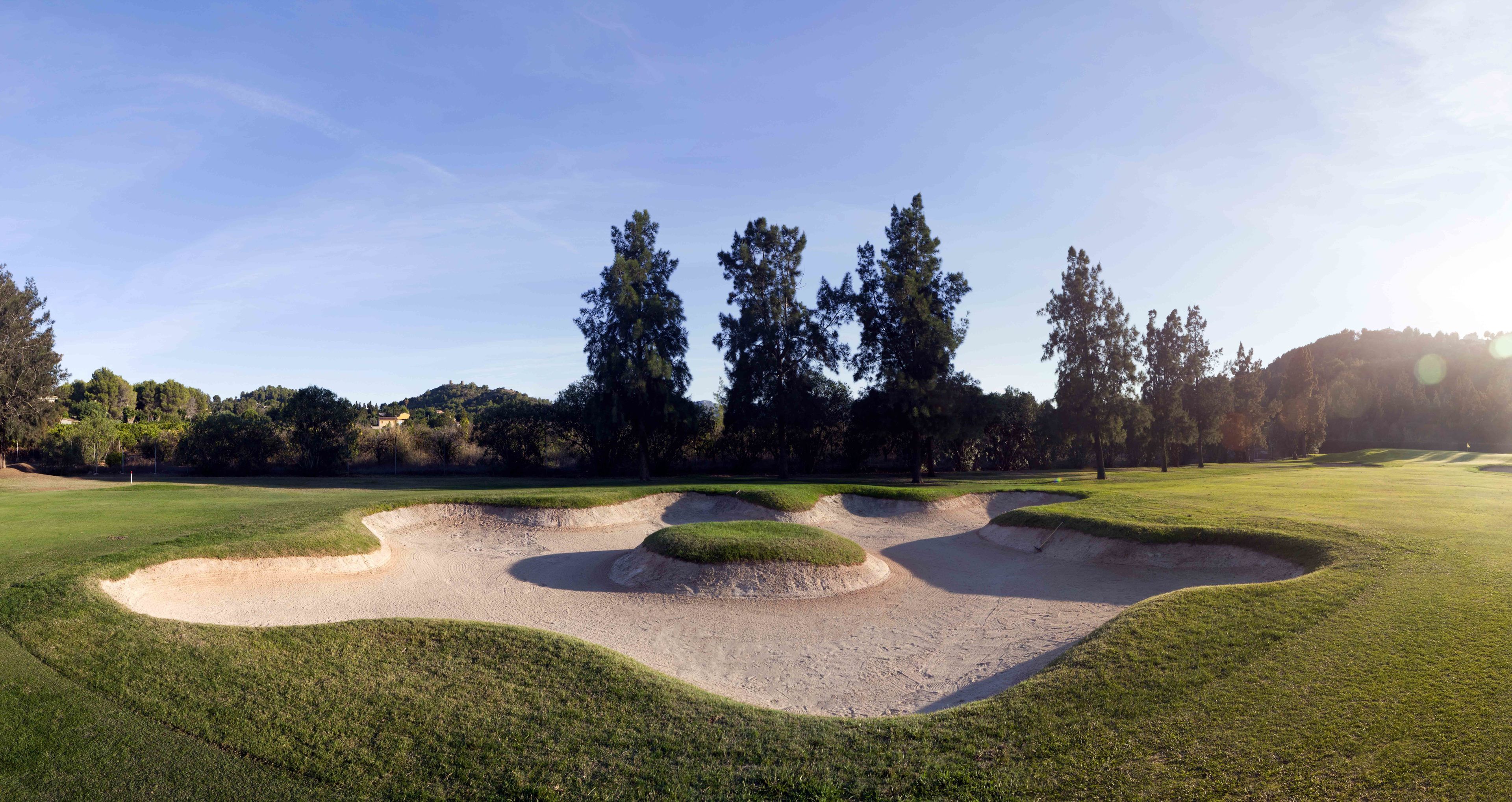 A golf course with sand bunkers and trees in the background.