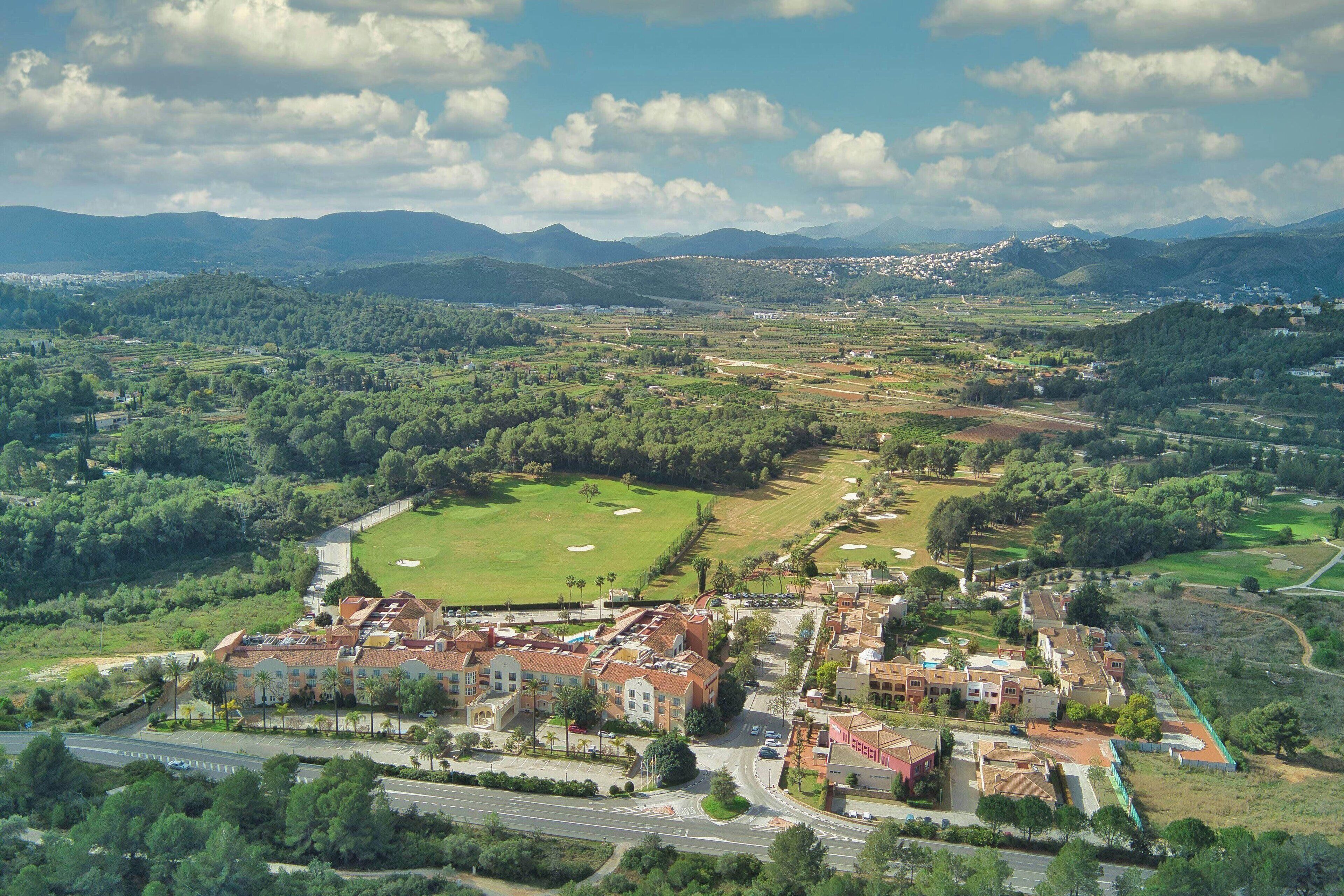 An aerial view of a town with a golf course, residential buildings, and surrounding greenery.