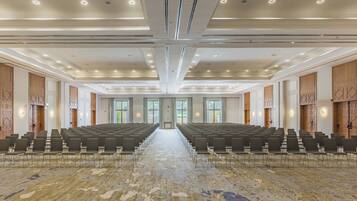 Een ruime congreszaal met rijen stoelen, een kamerbreed tapijt en een modern plafondontwerp.