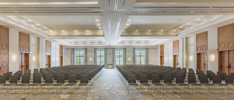 Une grande salle de conférence avec des rangées de chaises, une moquette à motifs et un design moderne au plafond.