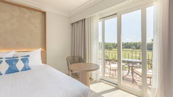 Habitación de hotel con una cama grande, una mesa redonda y un balcón con vistas a un paisaje verde.