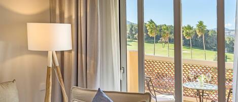 Une chambre d’hôtel avec un canapé, une lampe et une vue sur un terrain de golf, visible à travers une porte-fenêtre coulissante.
