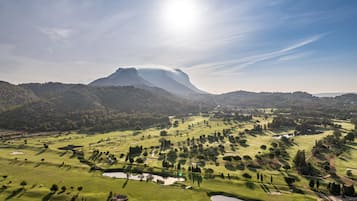 A golf course with a mountain in the background, surrounded by trees and water bodies.