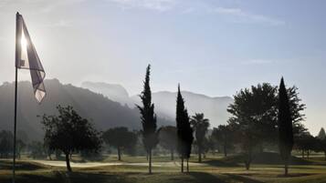 A golf course with a flag, trees, and mountains in the background.