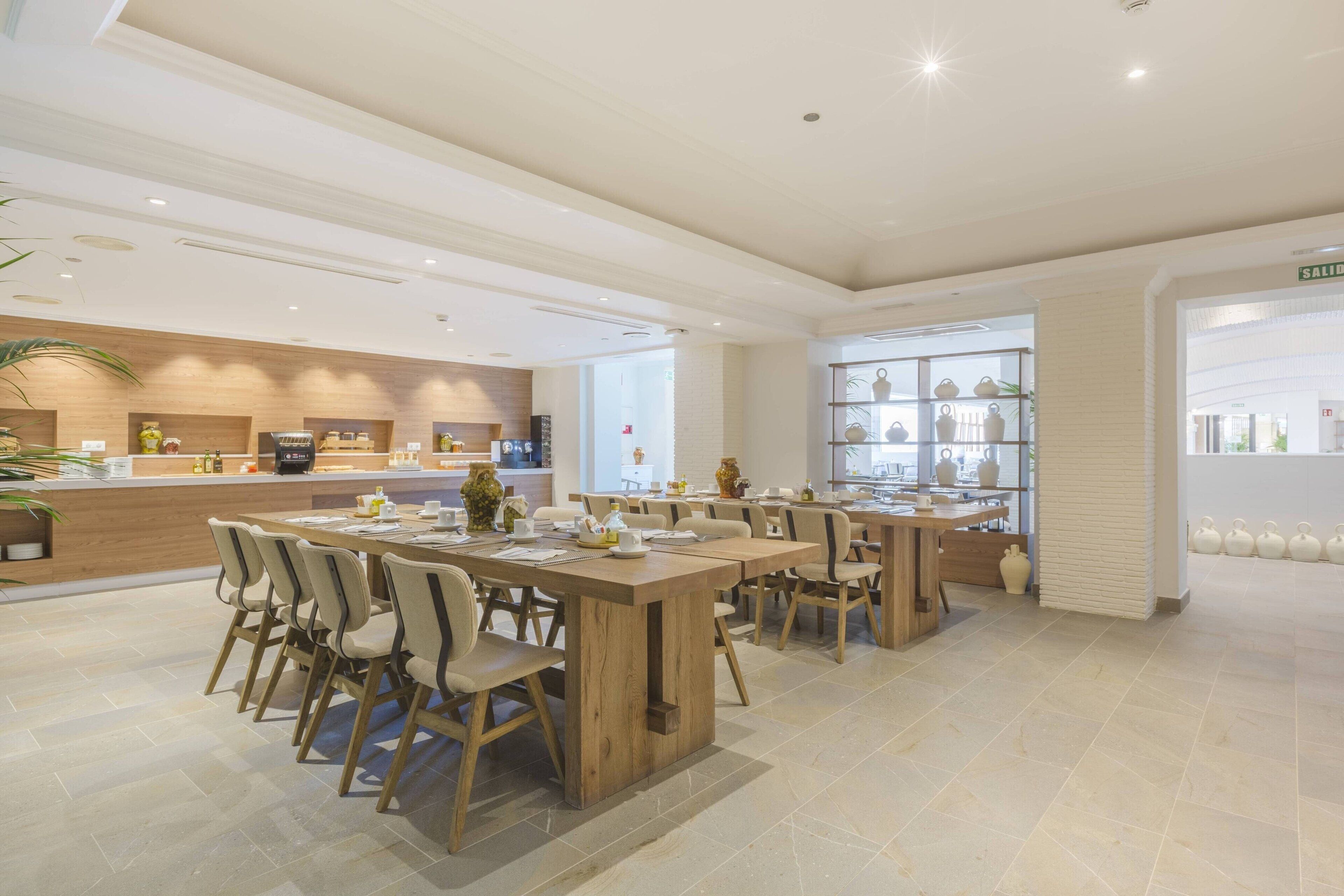 A modern dining area with wooden tables and chairs, a counter with a coffee machine, and shelves with decorative items.