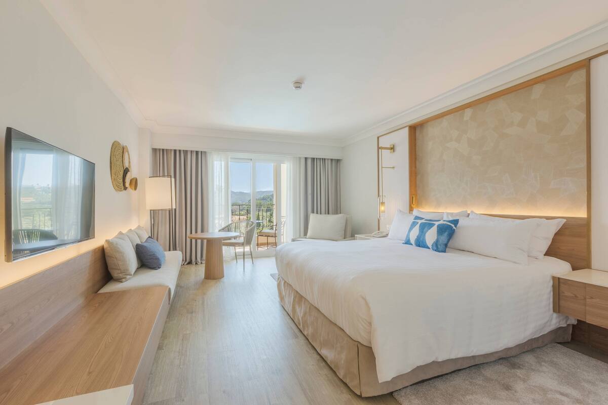 Quarto de hotel moderno com uma cama grande, televisão de tela plana, escrivaninha e vista para o exterior.