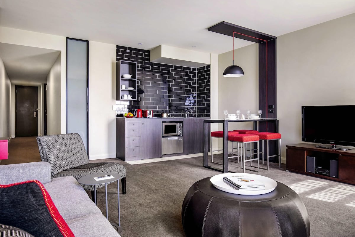 A modern living room with a sofa, ottoman, and a dining area with a TV and speakers.