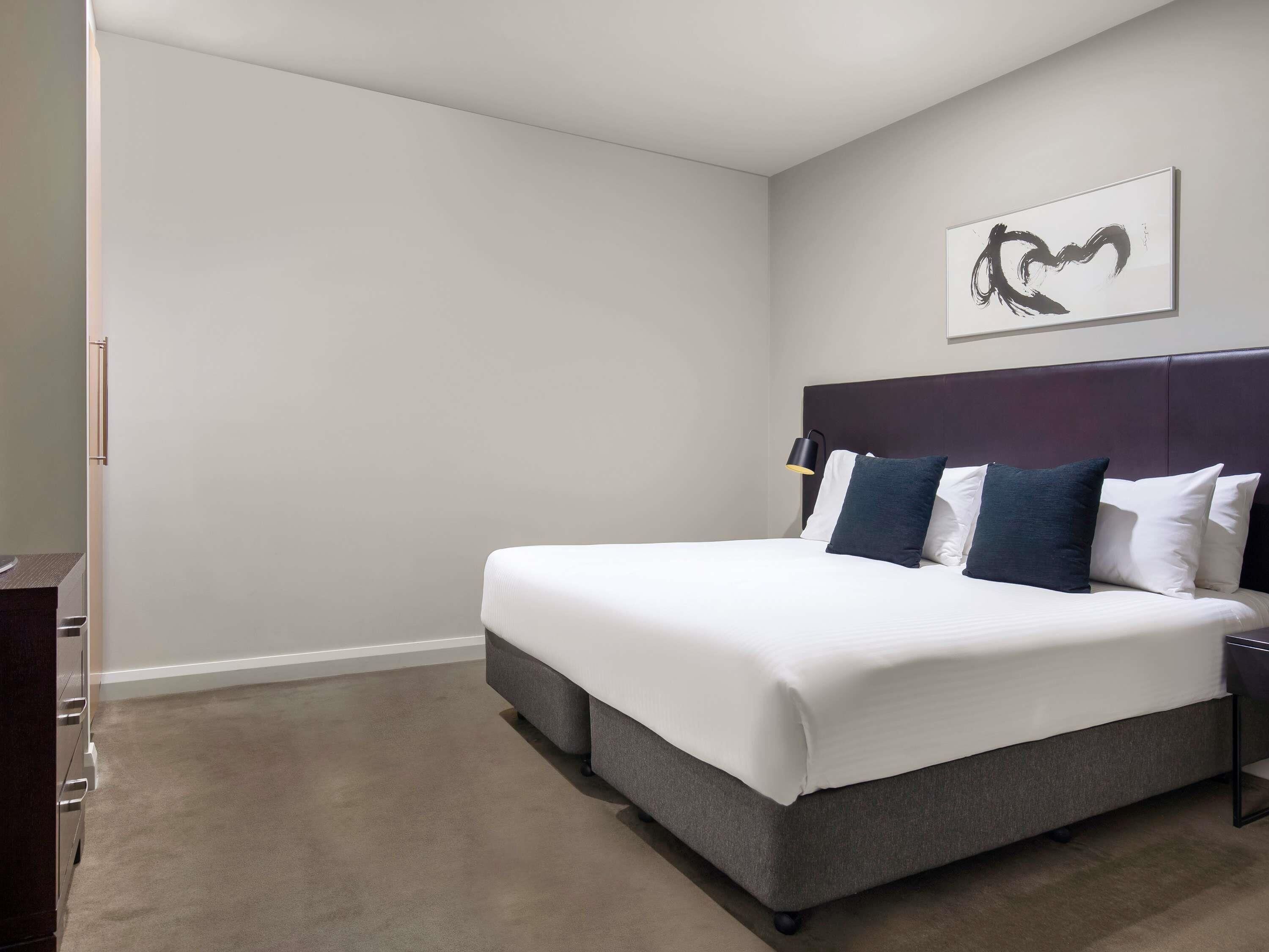 A neatly made bed with a dark headboard, a bedside lamp, and a wall-mounted artwork.