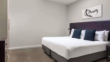 A neatly made bed with a dark headboard, a bedside lamp, and a wall-mounted artwork.