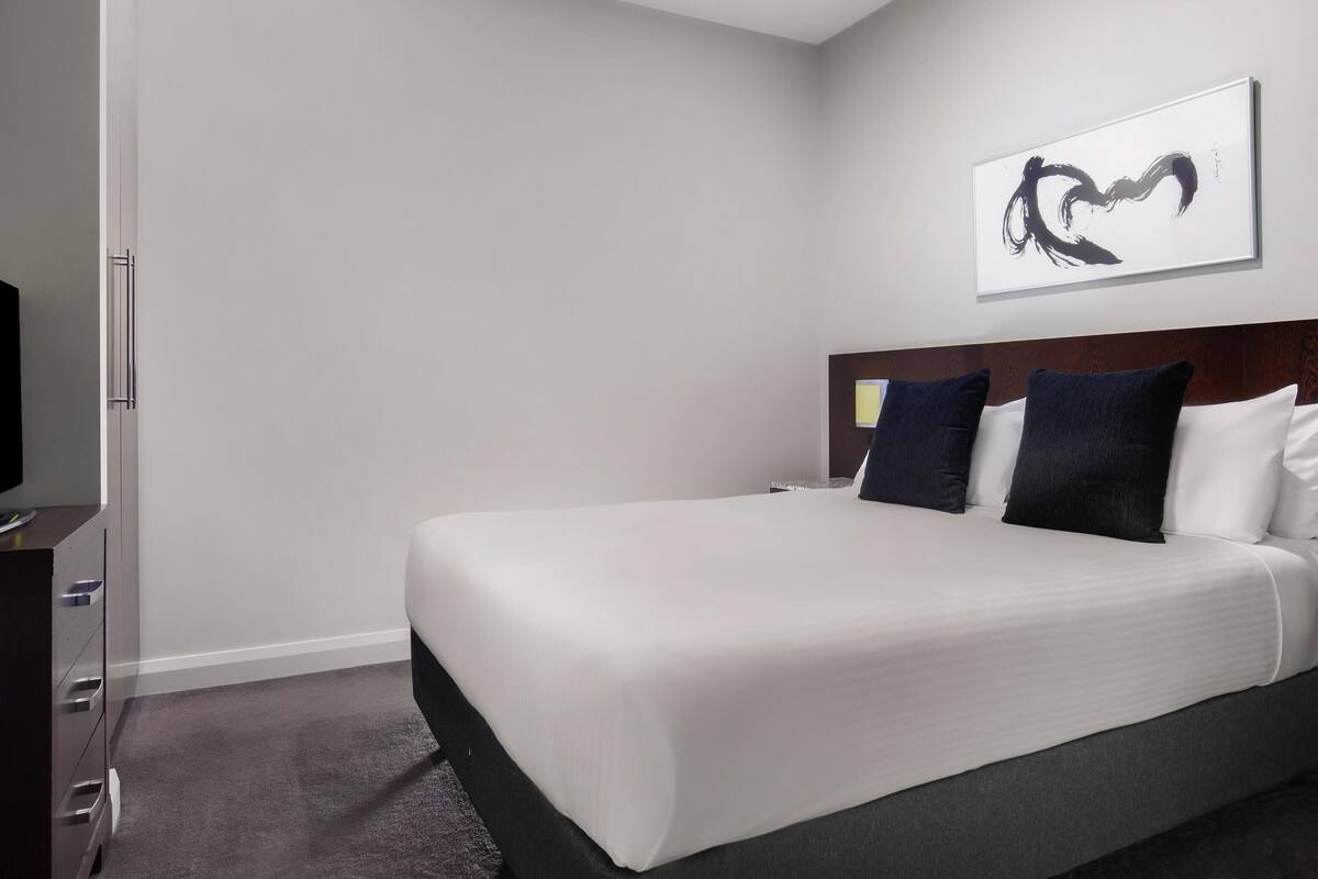 A hotel room with a bed, a television, a dresser, and a painting on the wall.