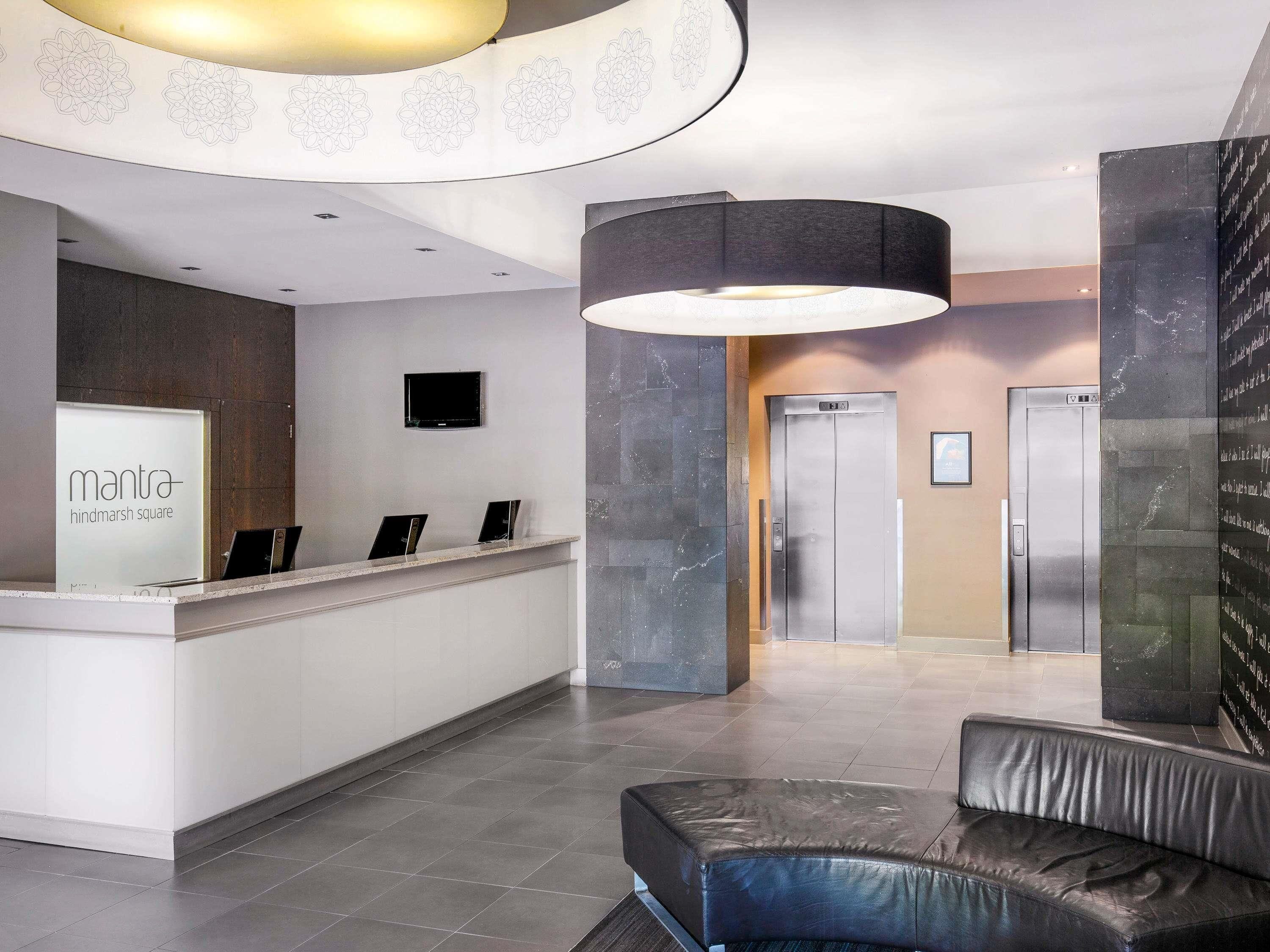 A reception desk with a sign, a flat-screen TV, a modern elevator, and a leather bench.