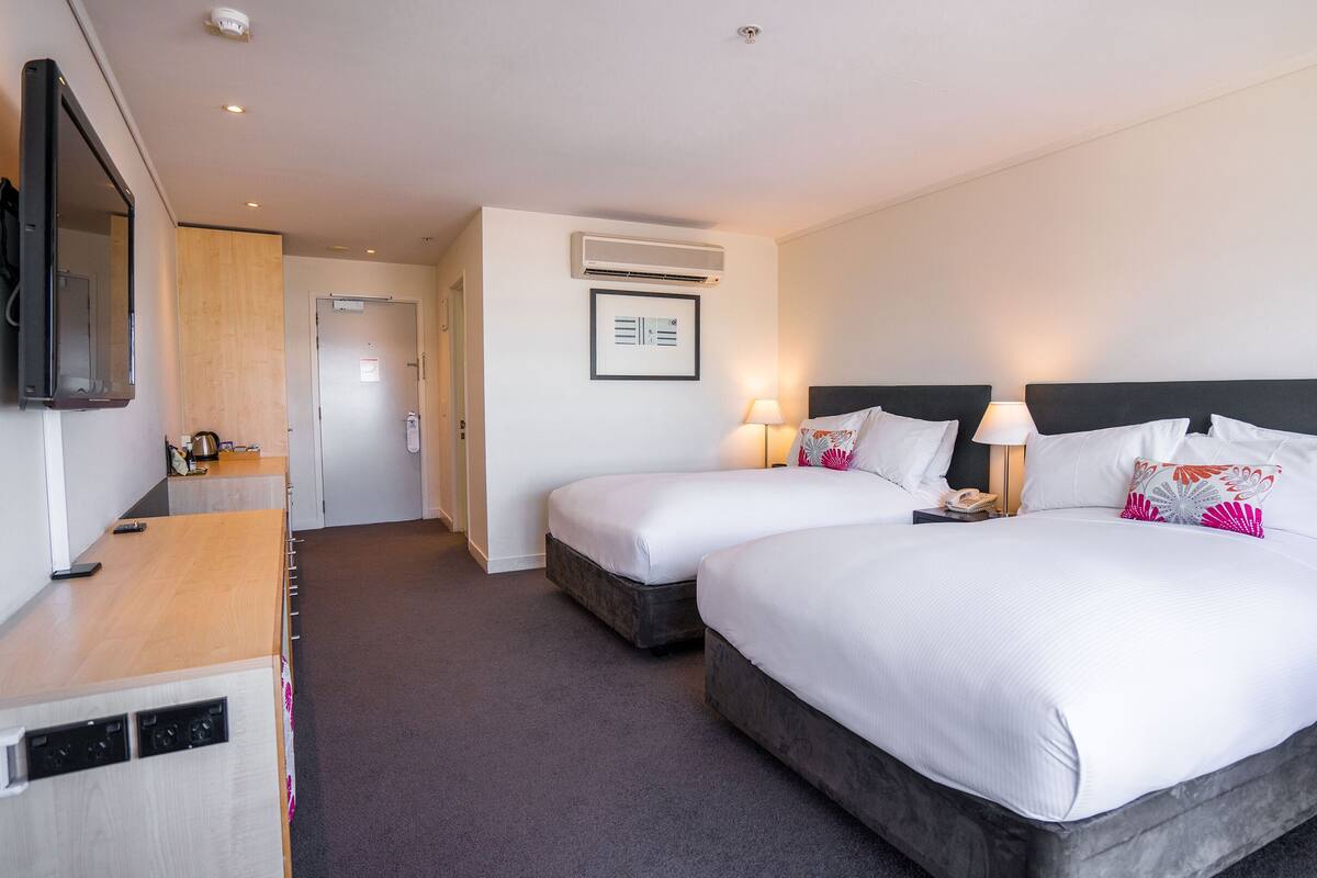 A hotel room with two beds, a TV, a desk, and a bathroom.