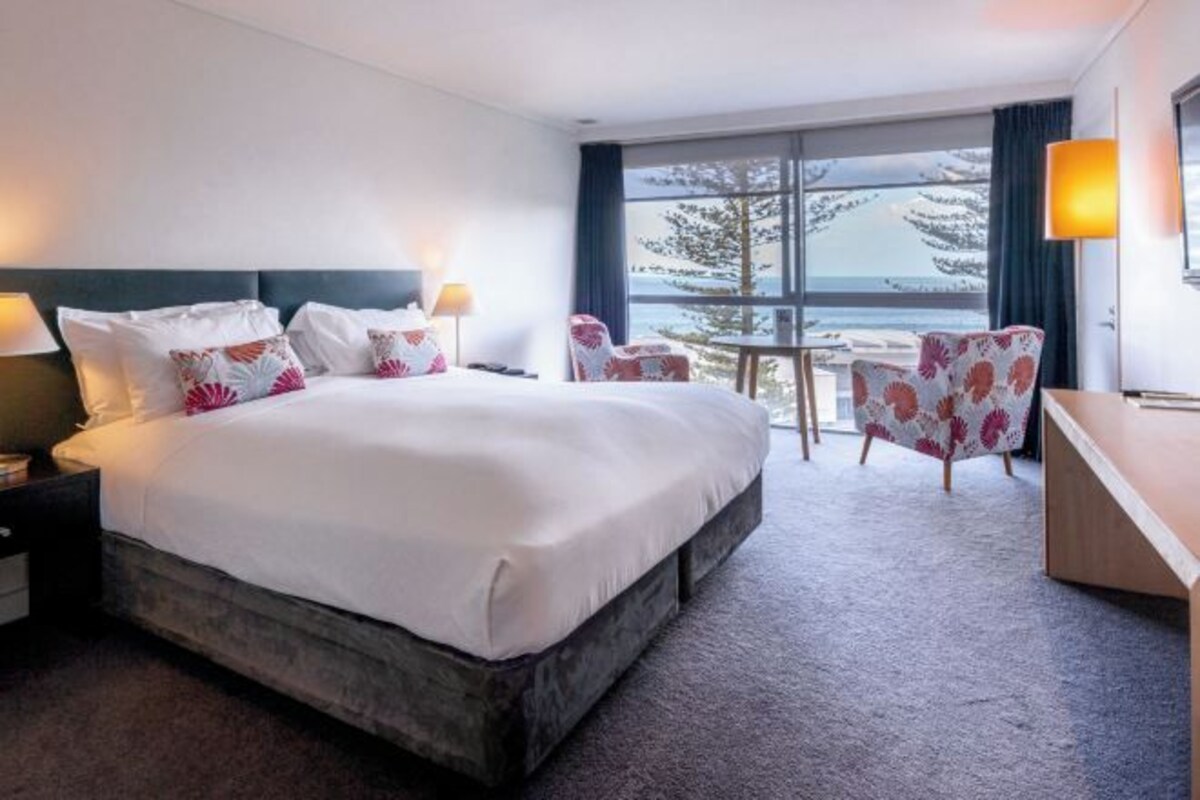 Habitación de hotel con una cama grande, dos mesitas de noche, un escritorio y una silla. Se ve una ventana con vistas a un paisaje nevado.