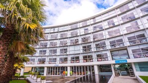 Un edificio moderno con fachada curva, amplios ventanales y una fuente de agua en primer plano.