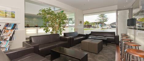 A modern hotel lobby with leather sofas, a coffee bar, and a large window offering a view of the street.
