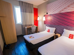 Een hotelkamer met twee bedden, een bureau, een stoel en een rode accentmuur.