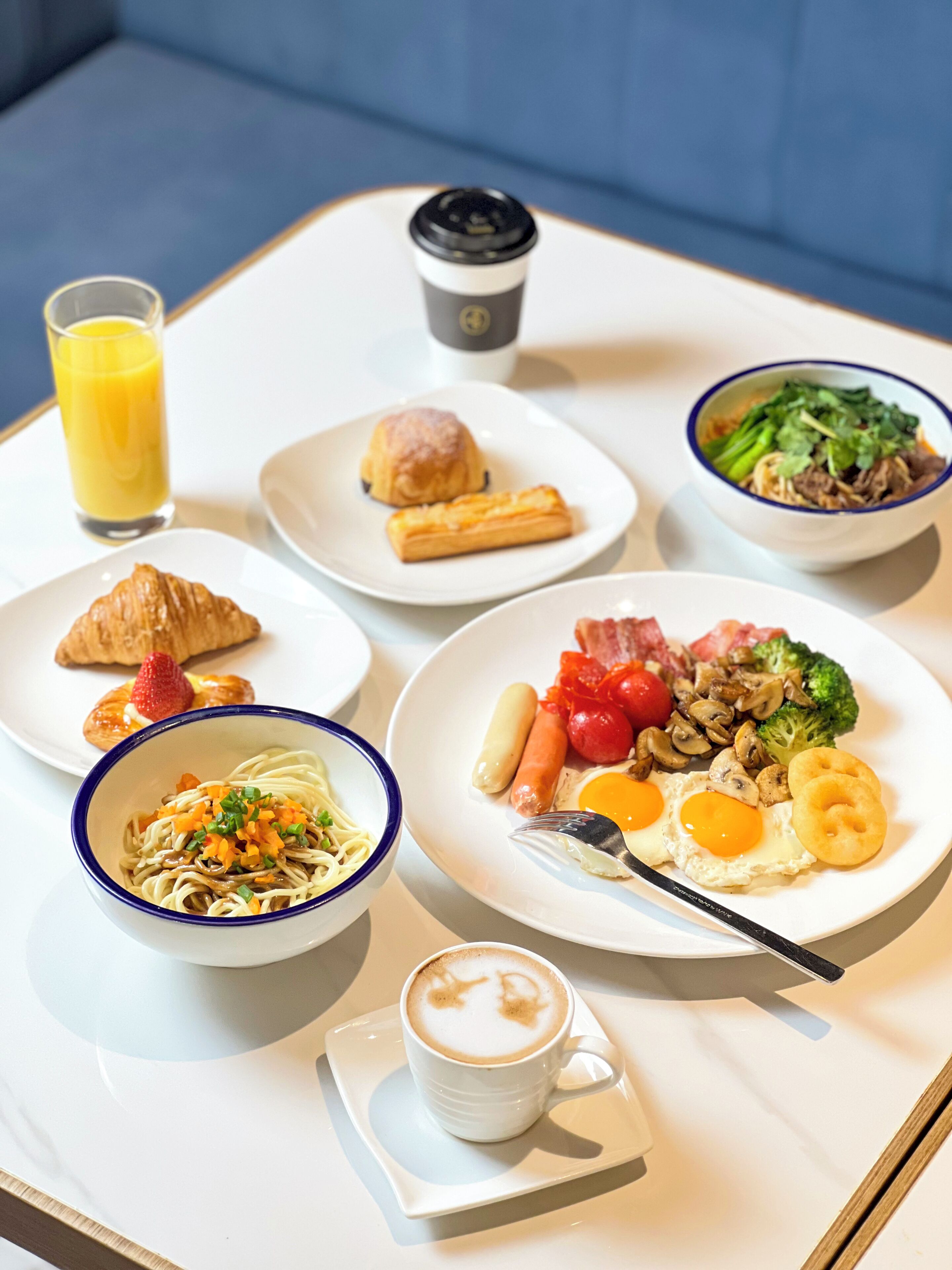 A breakfast tray with various dishes including eggs, sausages, and a bowl of noodles.