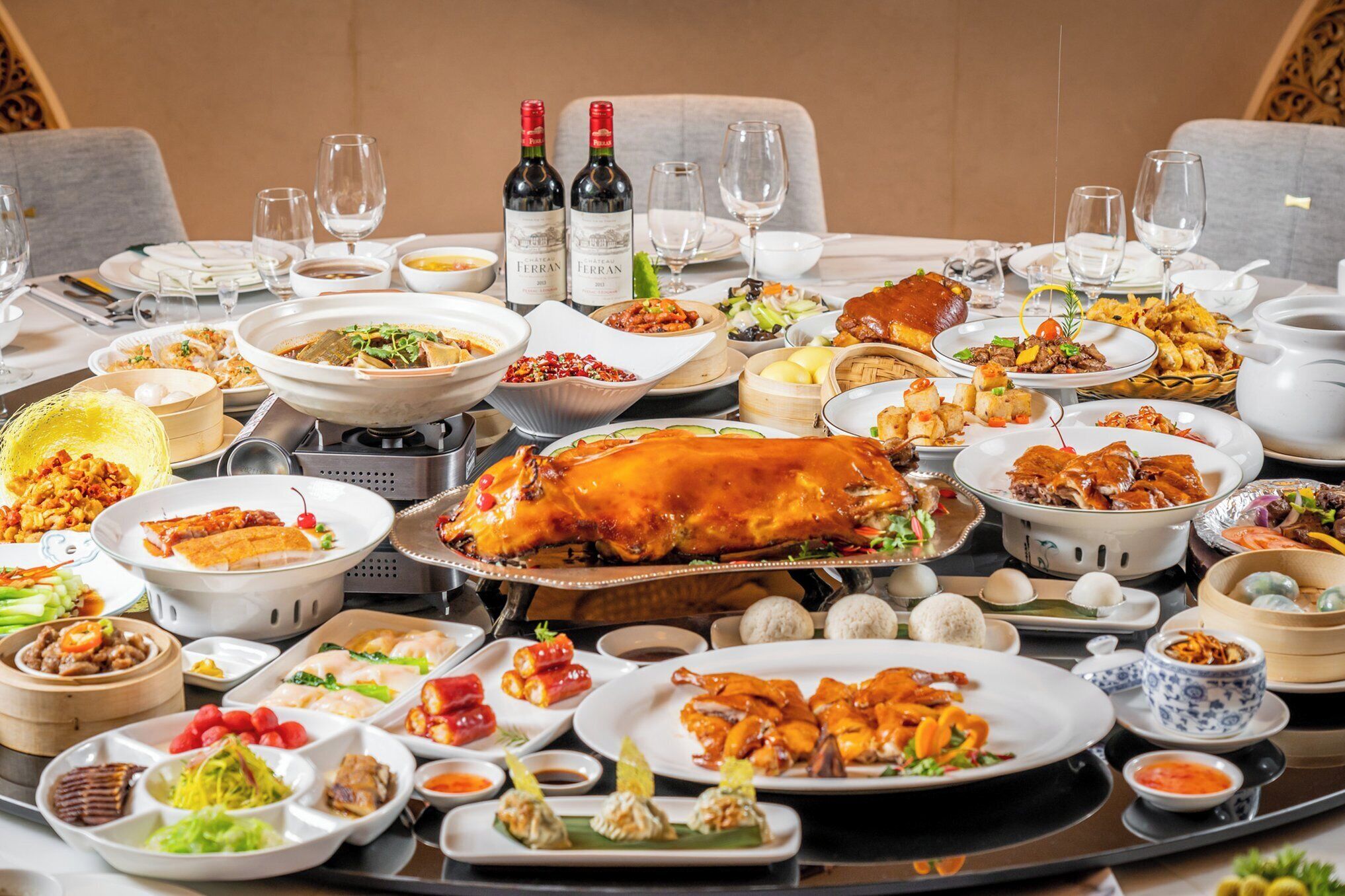 Een gedekte tafel met diverse gerechten, waaronder een gebraden kip, zeevruchten en groenten, plus wijnflessen en glazen.