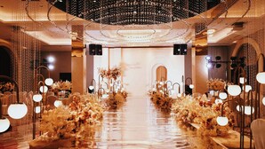 Un pasillo largo y reflectante con arreglos florales a ambos lados, que conduce a un escenario con un telón de fondo.