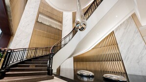 Un interior moderno con una escalera curva, paredes de mármol y una escultura reflectante.