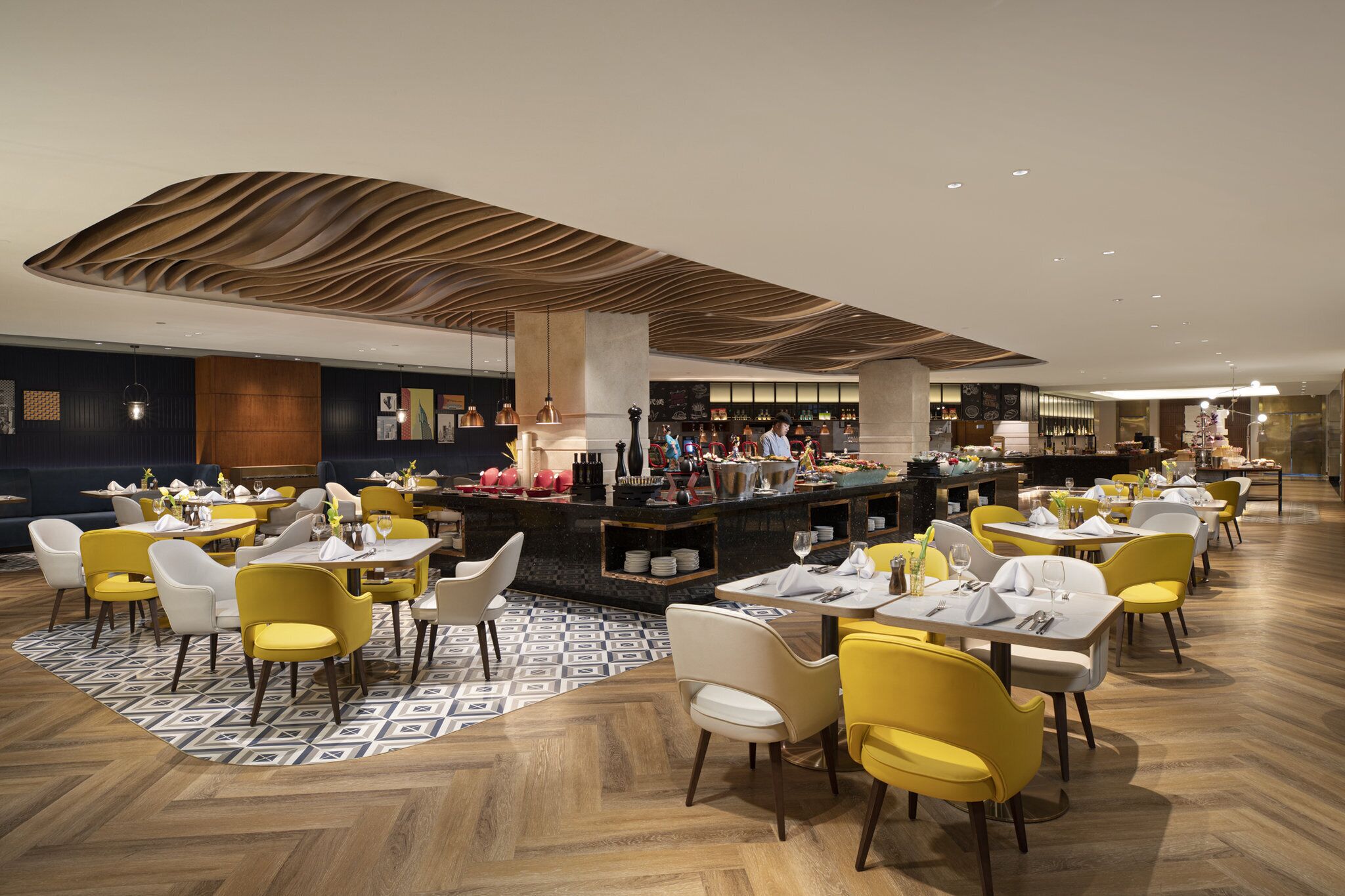 Un restaurante moderno con sillas amarillas y blancas, un tapete estampado y una zona de bar central.