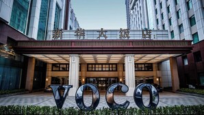 Entrada moderna de un hotel con grandes letras 'VOCO' al frente.