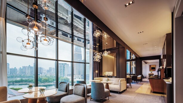 Un moderno vestíbulo de hotel con ventanas amplias, zonas de estar y un mostrador de recepción.