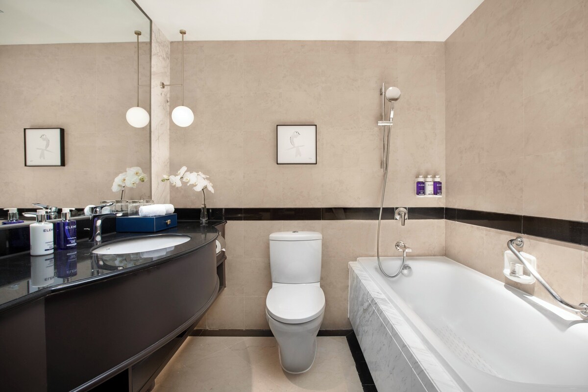 A modern bathroom with a black sink, white toilet, and a white bathtub. There are framed pictures on the wall, a mirror, and a shower with a handheld showerhead.