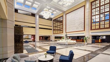 A spacious lobby with a high ceiling, chandeliers, a reception desk, and seating areas.