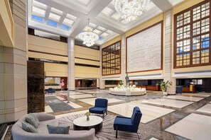 Eine geräumige Lobby mit hoher Decke, Kronleuchtern, einer Rezeption und Sitzbereichen.