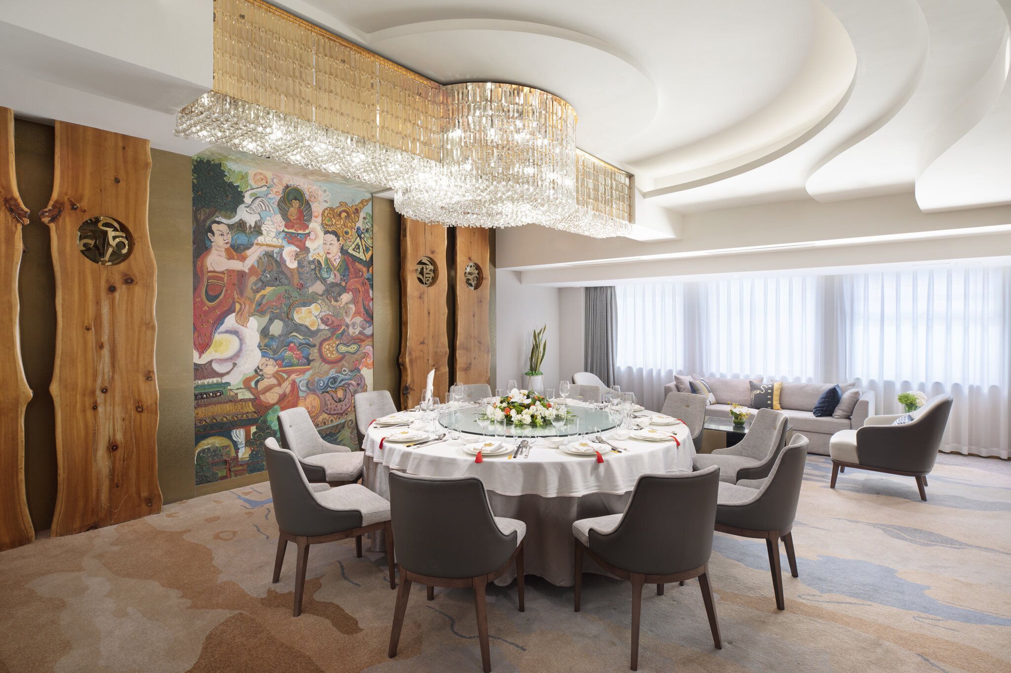 Un comedor con una mesa redonda dispuesta para seis comensales, rodeada de seis sillas, una araña y un mural en la pared.