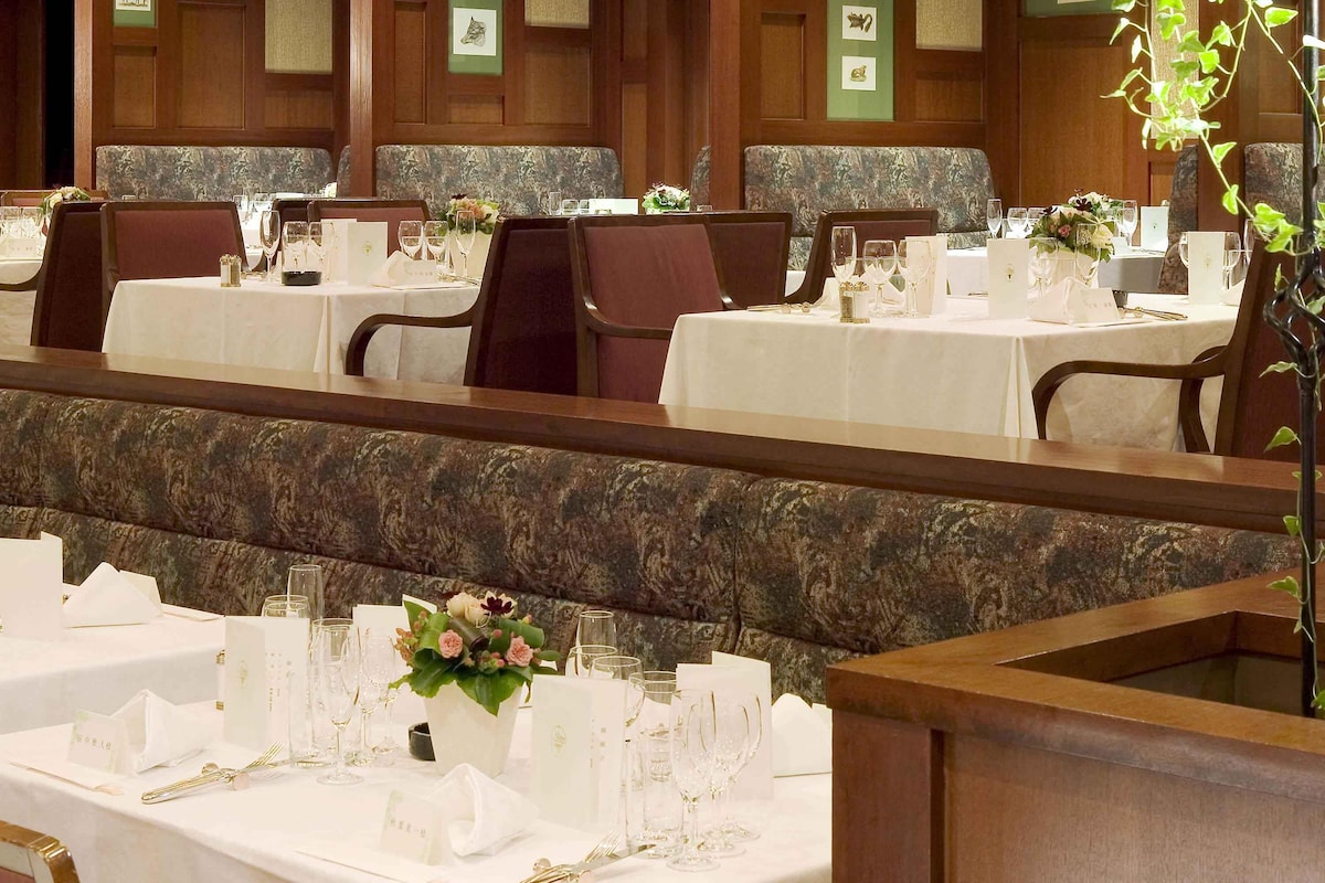 Un restaurante con varias mesas dispuestas para comer, cada una con manteles blancos, cristalería y centros de mesa florales.