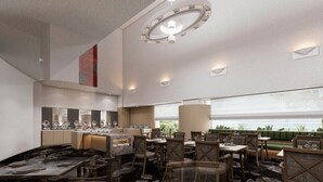 Un restaurante moderno con techos altos, una lámpara central y un área de estar con vistas a zonas verdes.