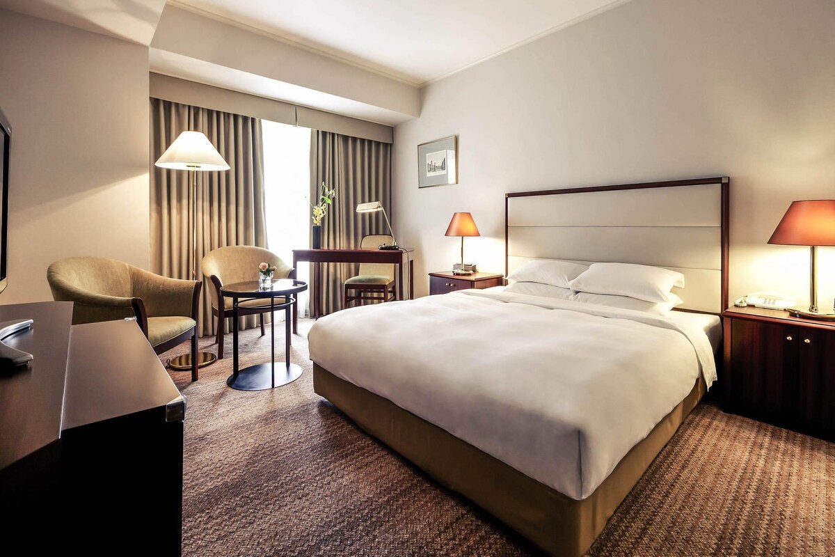 Ein Hotelzimmer mit einem großen Bett, zwei Stühlen, einem Schreibtisch, einer Lampe und einem Telefon.