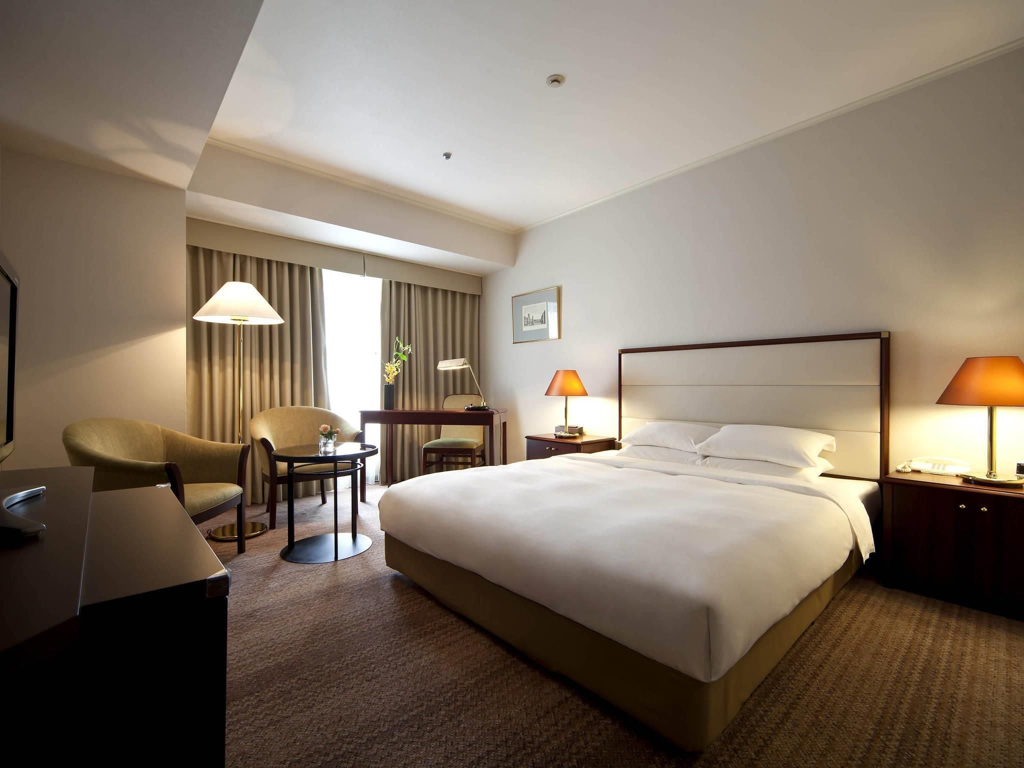 Habitación de hotel con una cama grande, un escritorio con silla, una mesita y dos lámparas.
