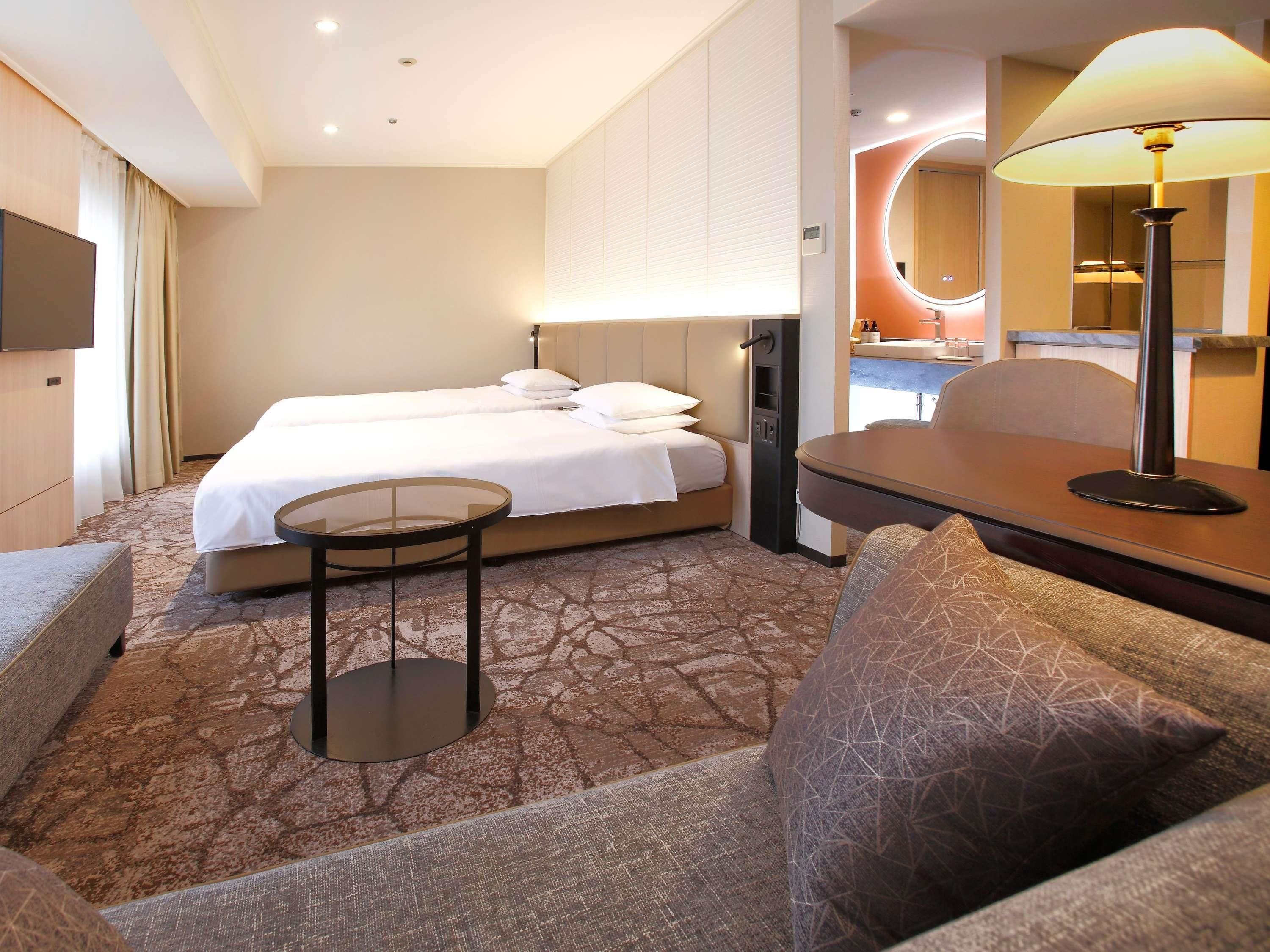 A hotel room with a bed, a small table, a sofa, and a lamp.