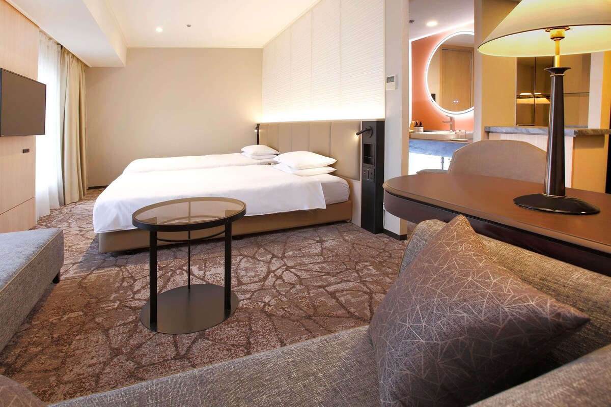 Ein Hotelzimmer mit Bett, einem kleinen Tisch, einer Couch und einer Lampe.