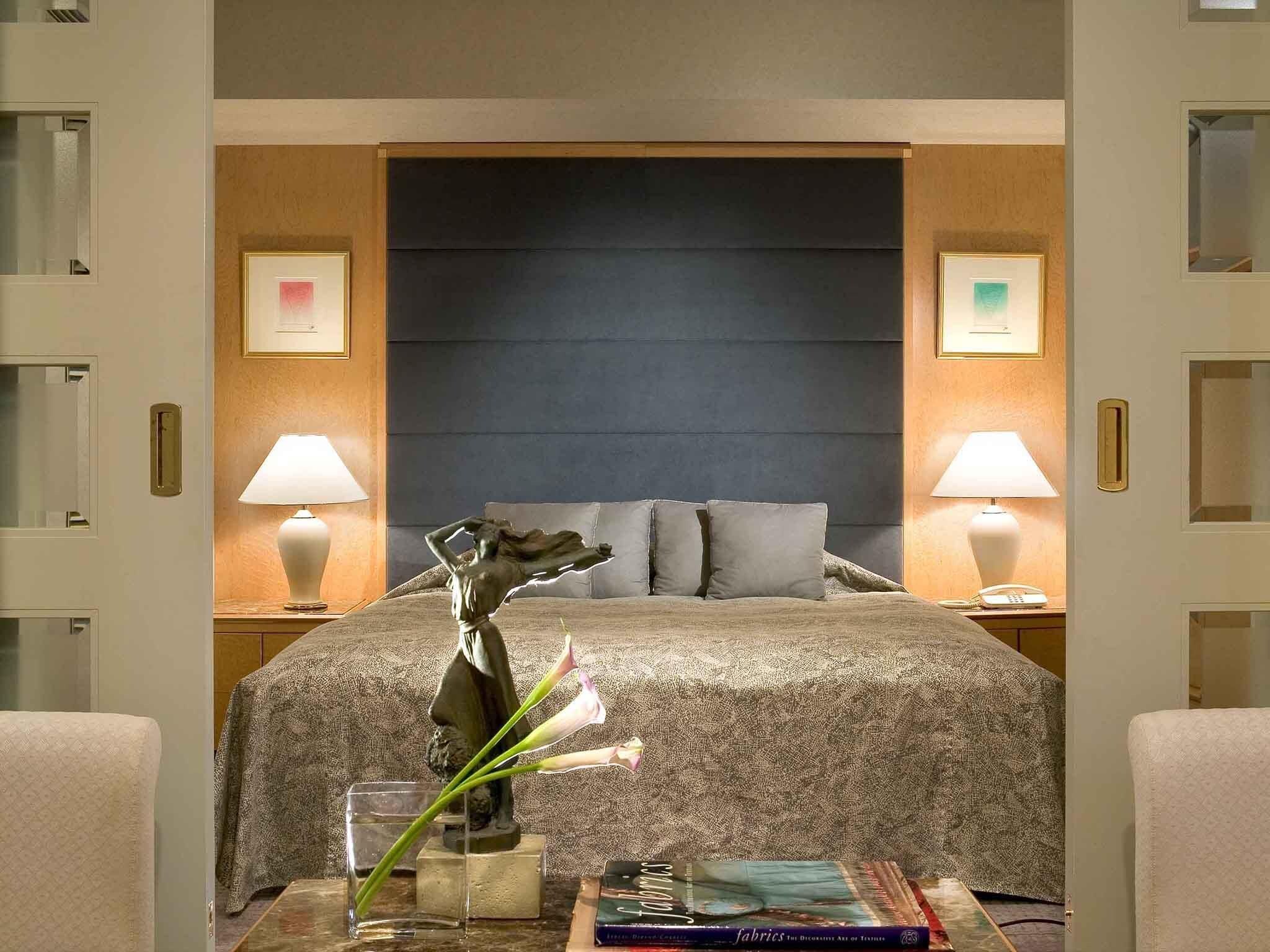 A hotel room with a bed, bedside lamps, a vase with flowers, a book, and a nightstand.